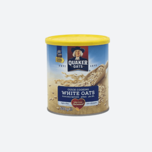 A 500g pack of Quaker Oats Quick Cooking White Oats, displayed on a clean kitchen countertop with a bowl of prepared oatmeal topped with fresh fruits and nuts, symbolizing health and nutrition.